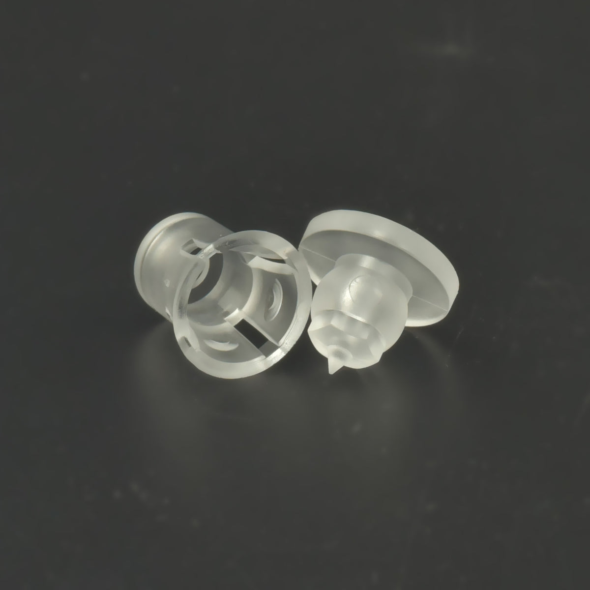 Două distanțiere transparente din plastic, așezate pe o parte, pe fundal închis.