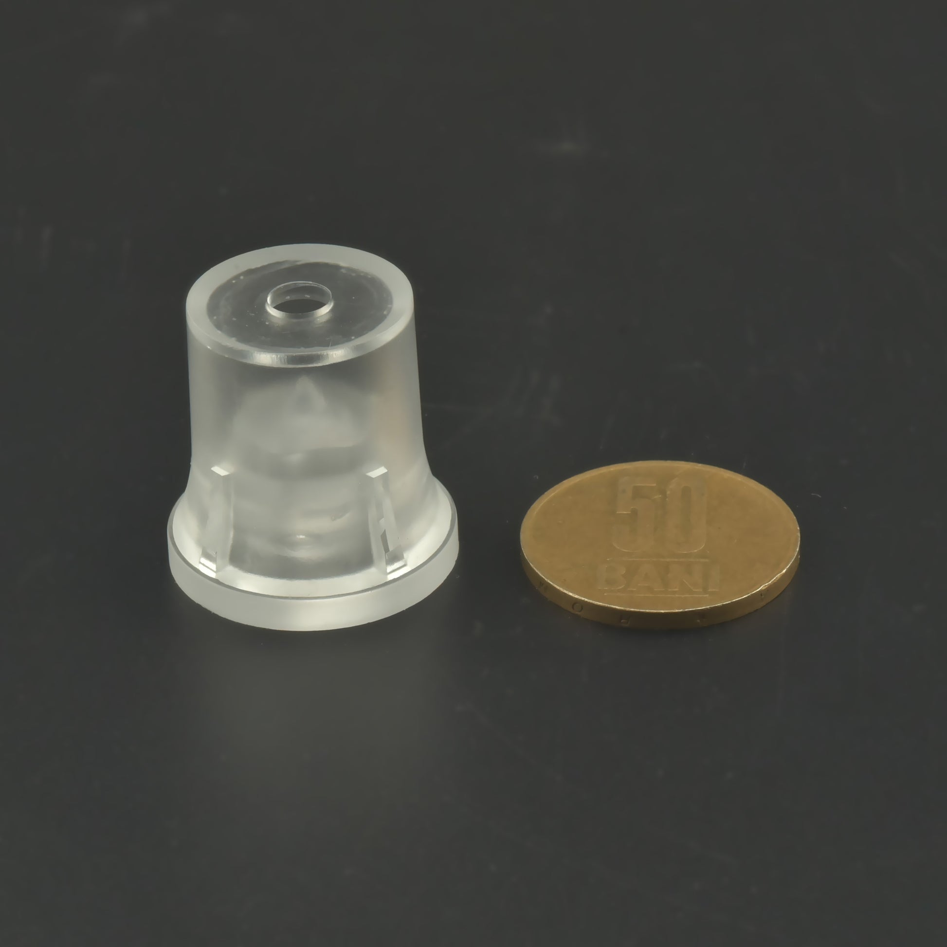 Distanțier cilindric transparent prezentat alături de o moneda.