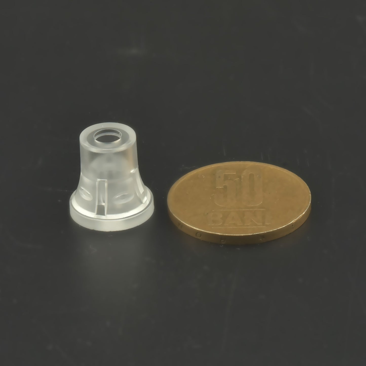 Distanțier din plastic transparent poziționat vertical lângă o moneda de 50 de bani.