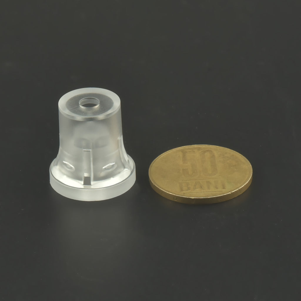 Distanțier cilindric transparent așezat vertical lângă o moneda de 50 de bani, pe fundal negru.