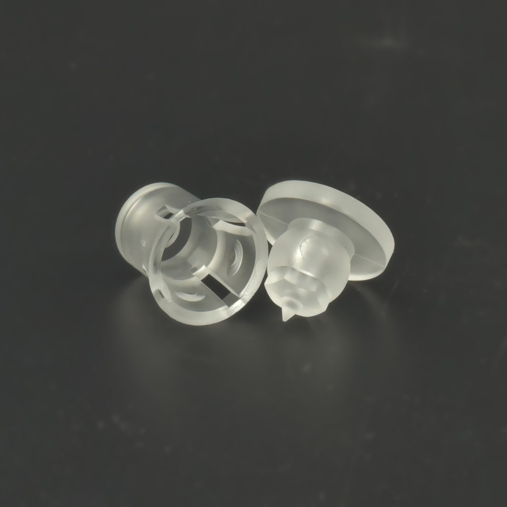Două distanțiere transparente din plastic, așezate pe o parte, pe fundal închis.